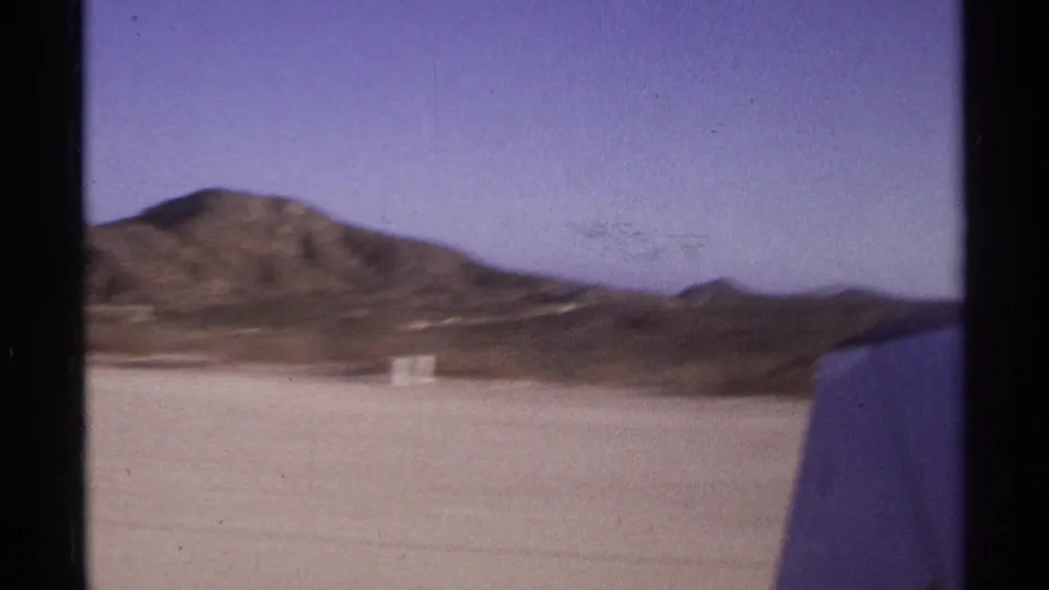8mm travel footage shows the aircraft wing at the edge of frame with runway surface and dry mountain ridges in Cabo San Lucas.
