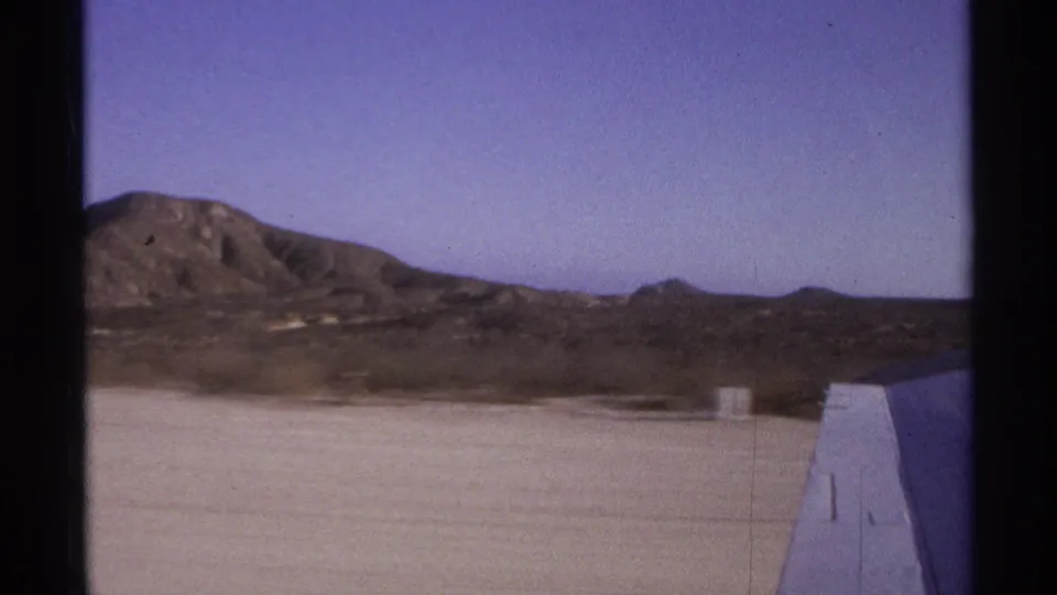 Late takeoff frame from a 1974 Cabo San Lucas home movie, showing the wing, runway, and broad dry mountain backdrop.