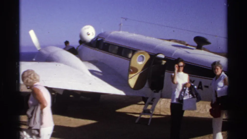 In 1974 Cabo San Lucas footage, two women with handbags pose near a small white propeller plane with an open door.