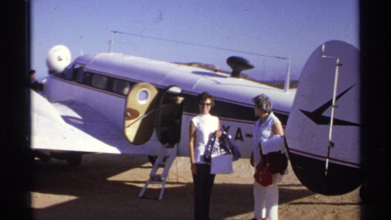 Two women stand in front of the plane's open door and large tail section.