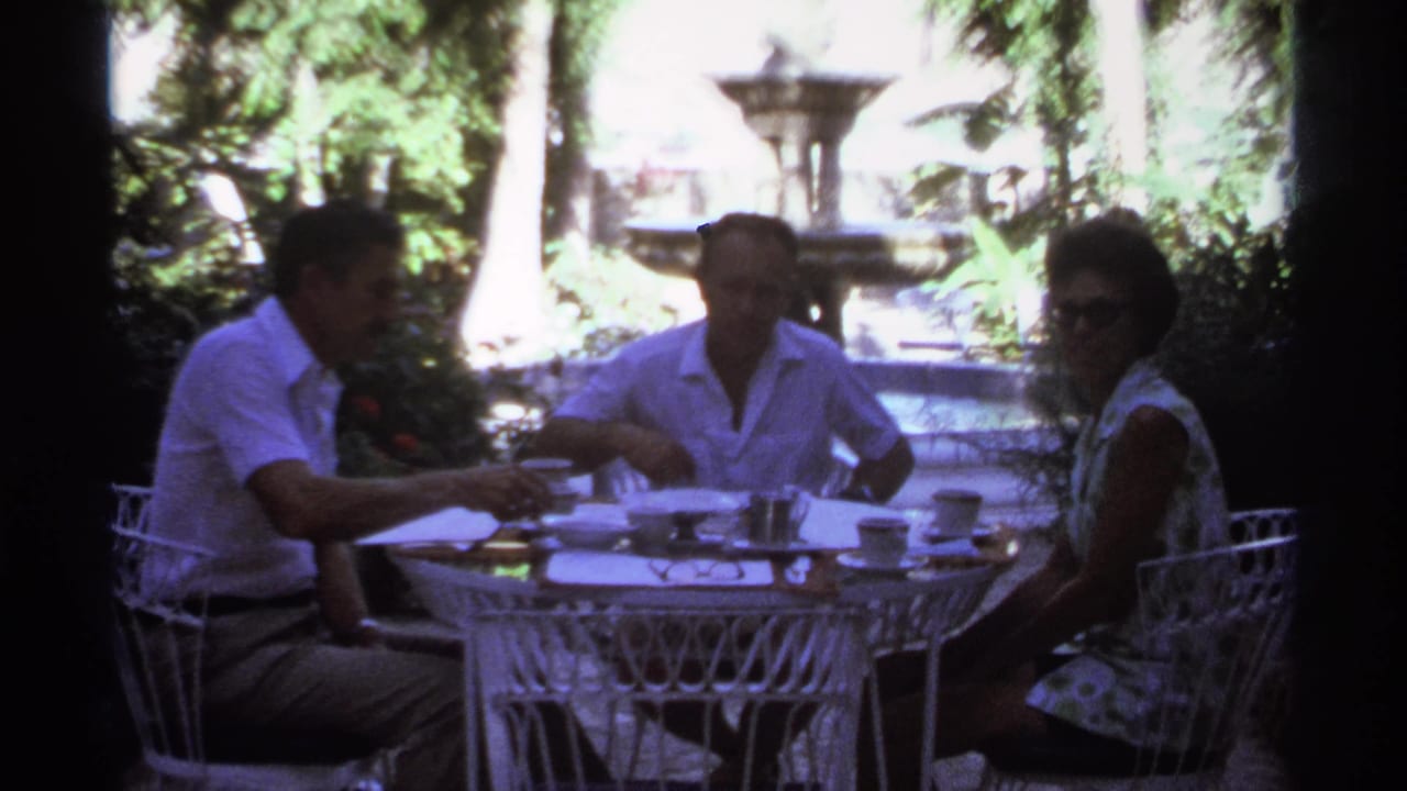 Adults seated at an outdoor table in a shaded garden with a fountain visible behind them.
