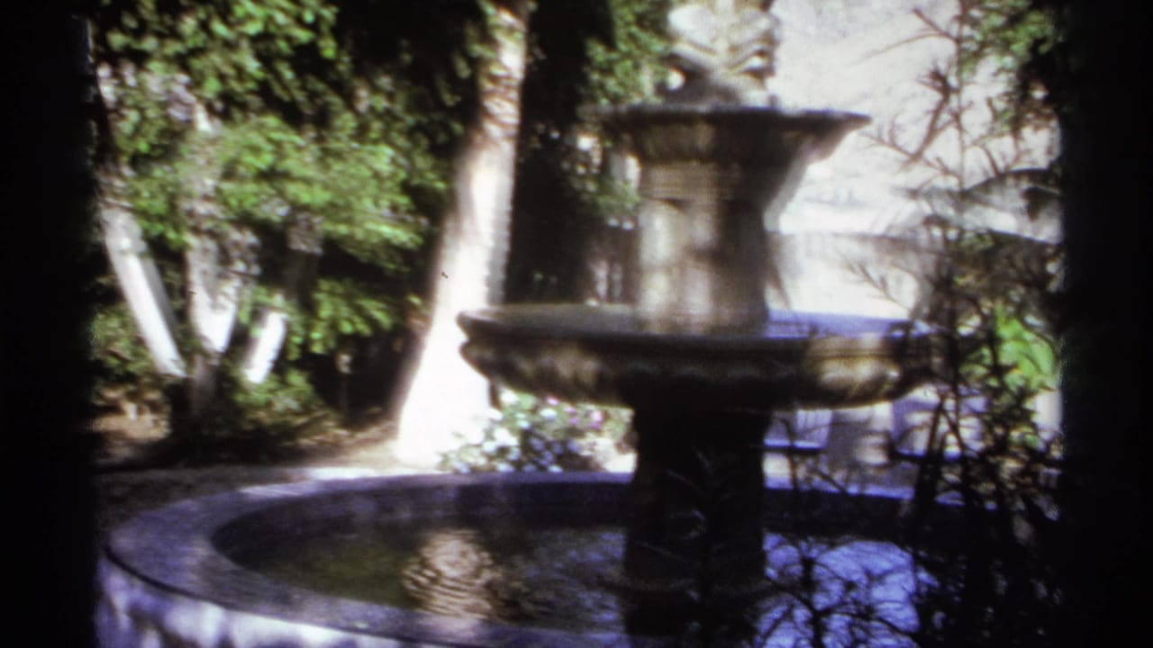 Tiered stone fountain in a shaded garden with trees and a circular basin.