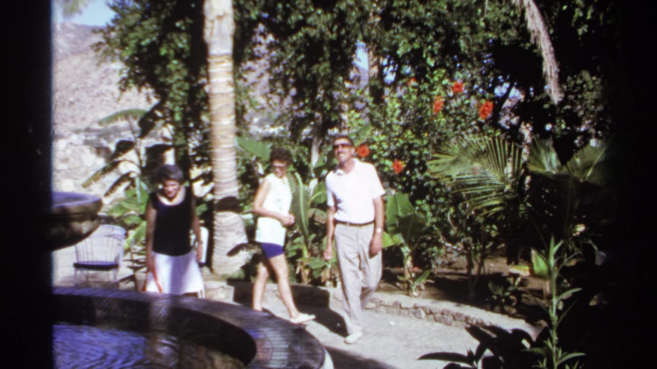 Three adults walking beside a circular fountain in a tropical garden.