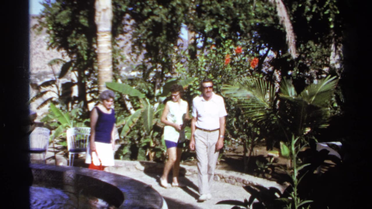 Three adults walking toward the camera through a sunny garden path.