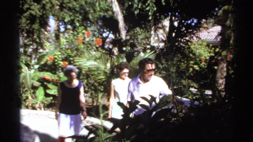 Adults in summer clothing walk through a sunlit garden in 1974 Cabo San Lucas home-movie footage.