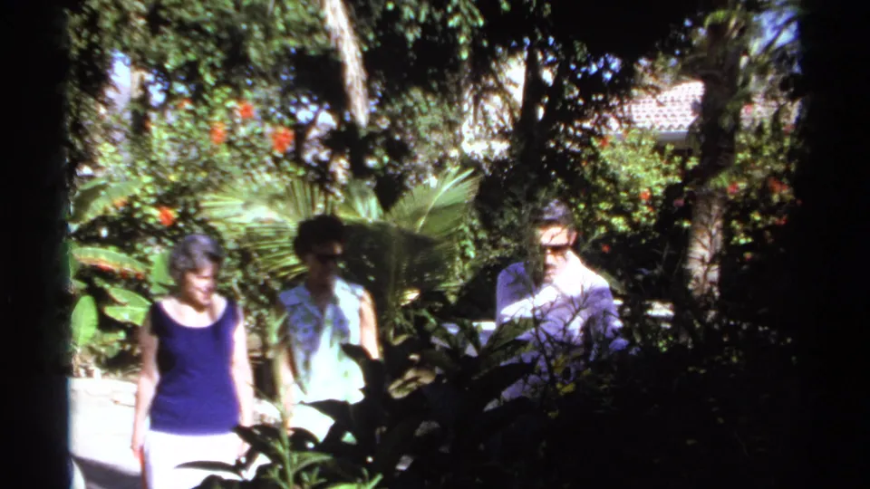 A woman in a navy sleeveless top leads as two others follow through a Cabo San Lucas garden in 1974 footage.
