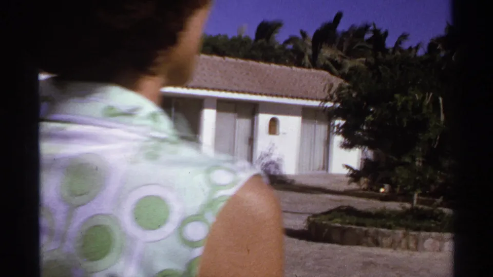 A woman in a patterned sleeveless top crosses close to the 8mm camera, partly obscuring a white Cabo San Lucas resort building and palms.