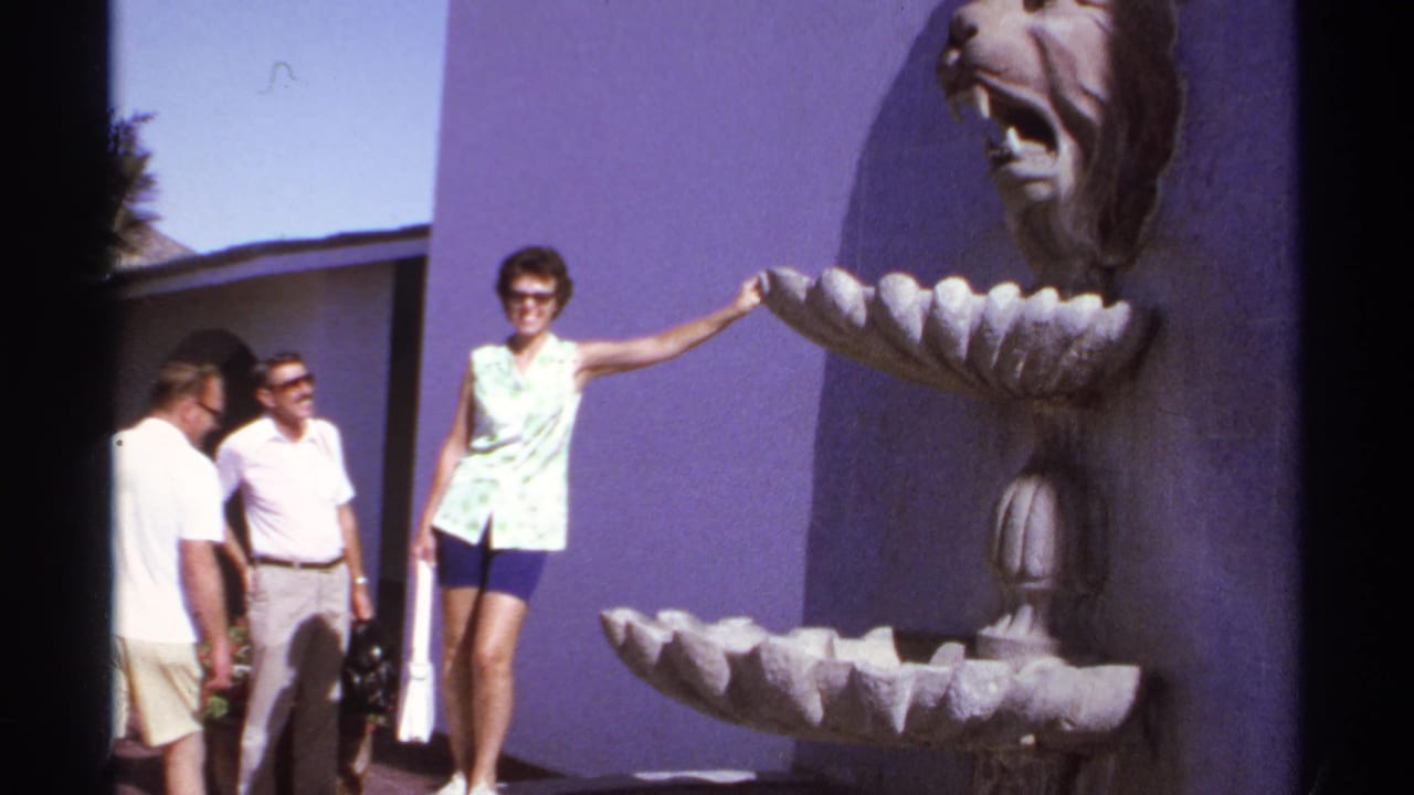 1974 Cabo San Lucas home-movie frame of a woman posing by a lion-head fountain with two men nearby.