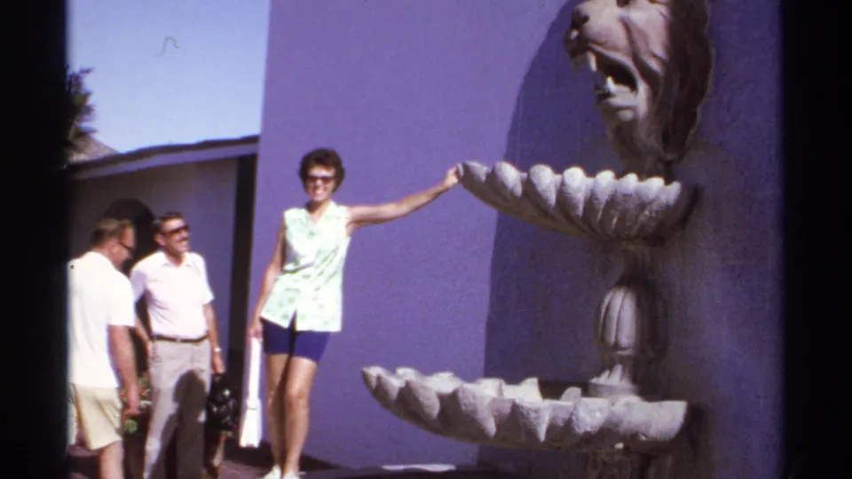 1974 Cabo San Lucas home-movie frame of a woman posing by a lion-head fountain with two men nearby.