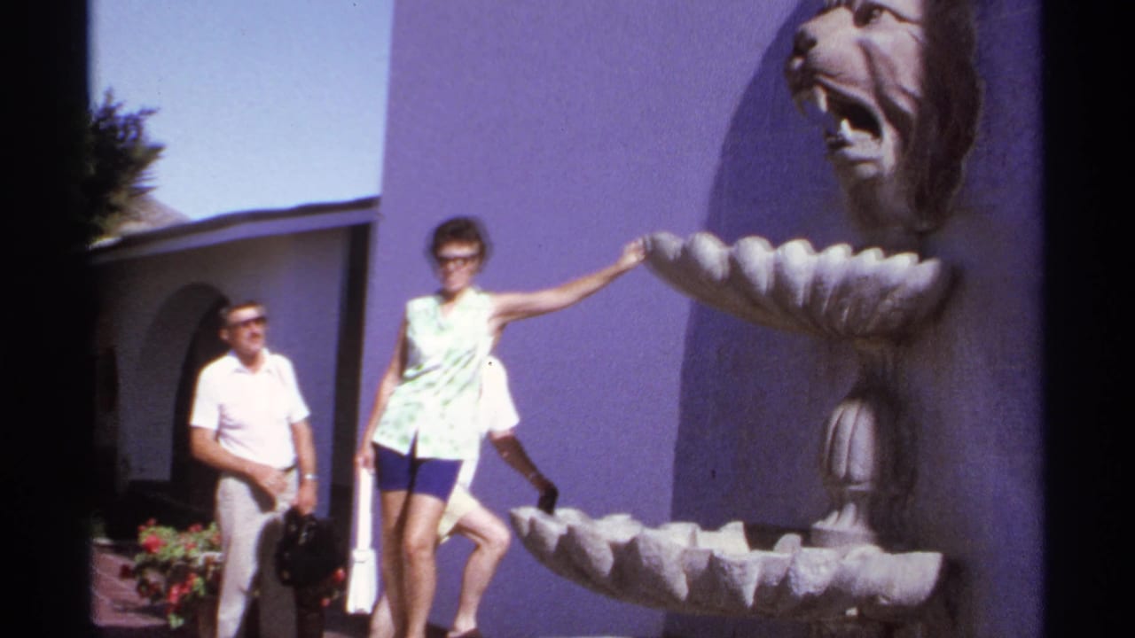 Woman rests one hand on the fountain edge as a man stands near the purple wall.