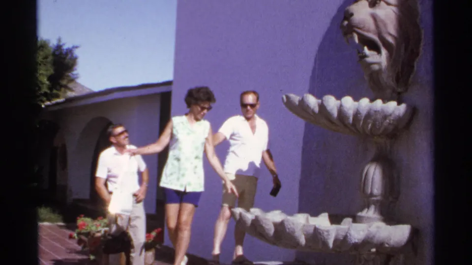 1974 Cabo San Lucas home-movie frame of a woman moving near a lion-head fountain with two men in sunglasses close by.