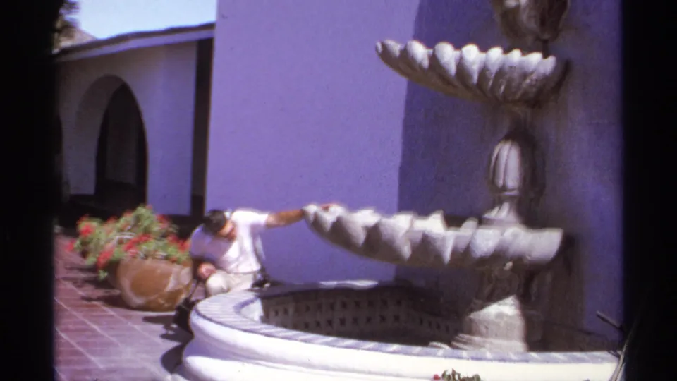 The 1974 Cabo San Lucas clip shows a man crouching beside the lower basin of a decorative fountain in bright sun.