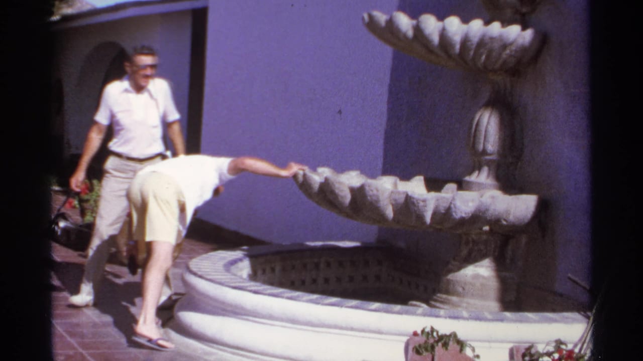 One man bends toward the fountain basin while another man stands beside the wall.