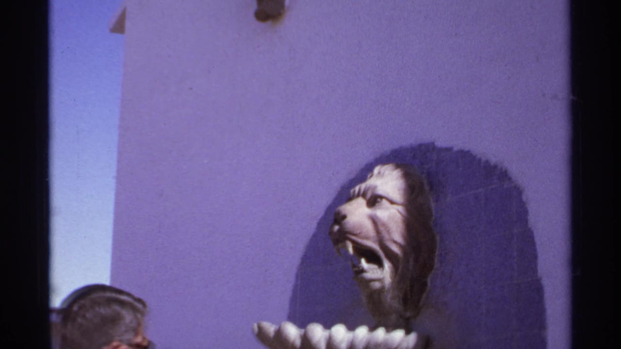Lion-head sculpture on a purple wall with the tops of visitors' heads at the bottom edge.