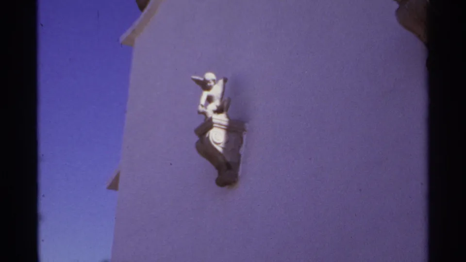 Cabo San Lucas 1974 home-movie frame showing a sunlit white stucco wall with a small decorative figure and dark film borders.