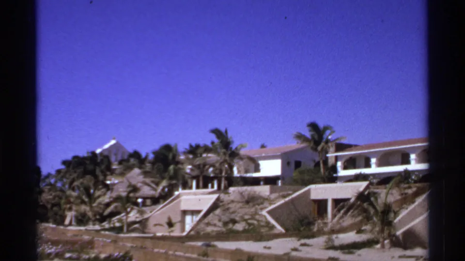 A brief Cabo San Lucas resort view shows white buildings, palms, slopes, and bright blue sky after the garden pose.