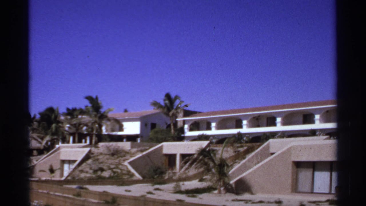 1974 Cabo San Lucas frame of a white modernist resort complex with arched balcony openings, palms, and terraced hillside units.