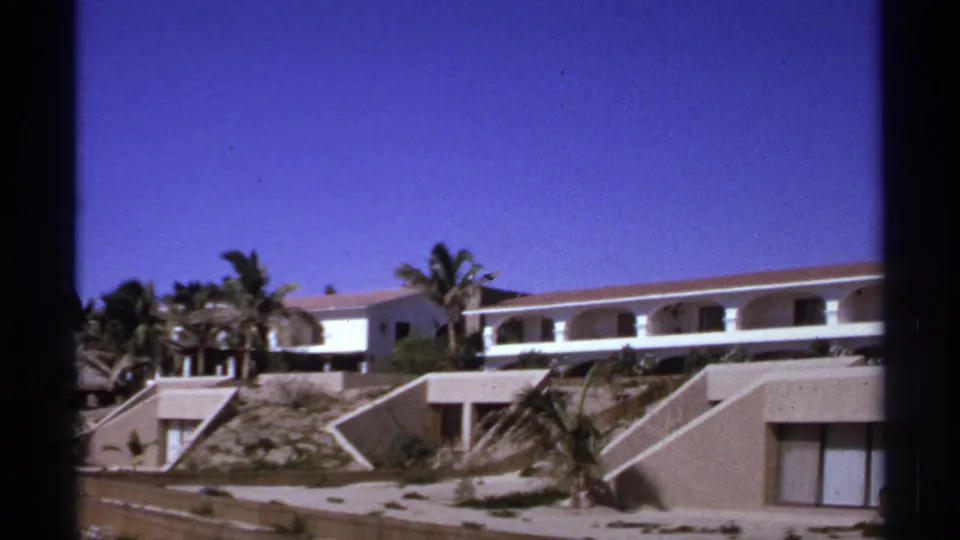 1974 Cabo San Lucas frame of a white modernist resort complex with arched balcony openings, palms, and terraced hillside units.