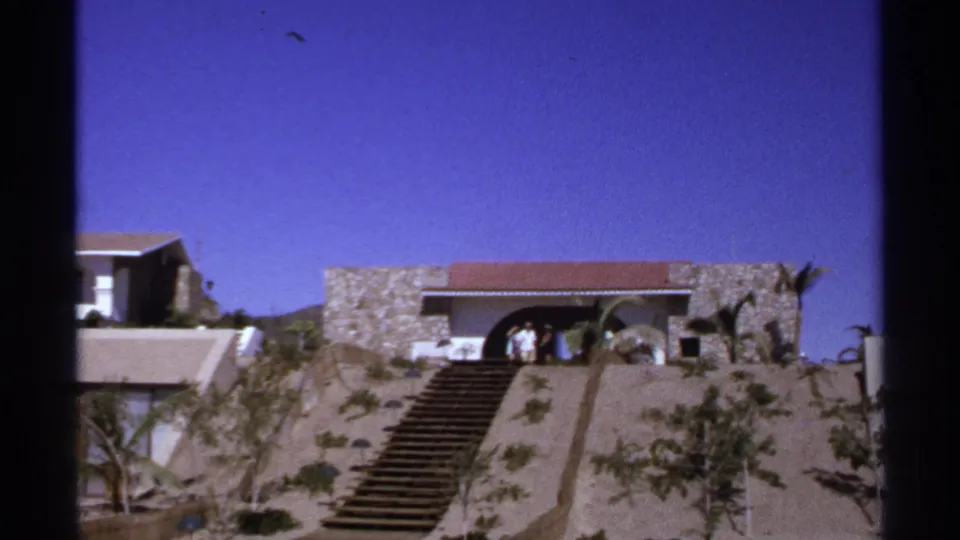 1974 Cabo San Lucas home-movie frame centered on the staircase rising toward a stone building with people by the entry.