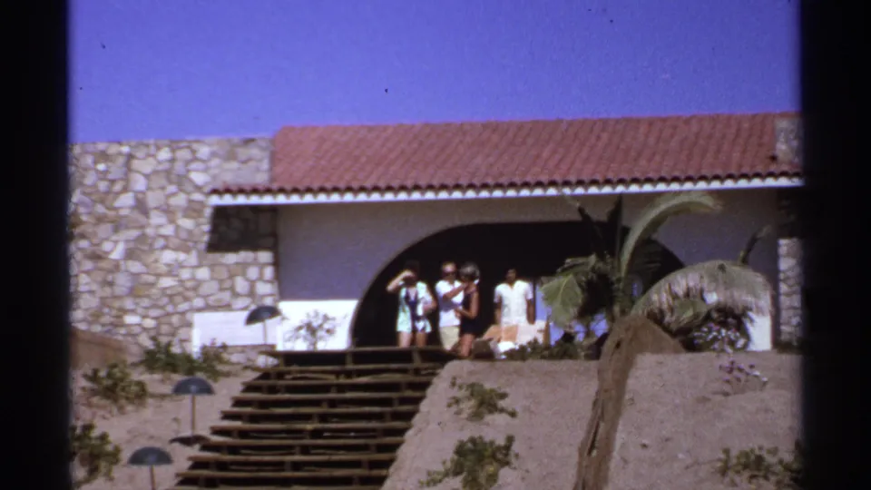 Several vacationers look toward the camera from the top of a long staircase outside a 1970s hillside house in Cabo San Lucas.