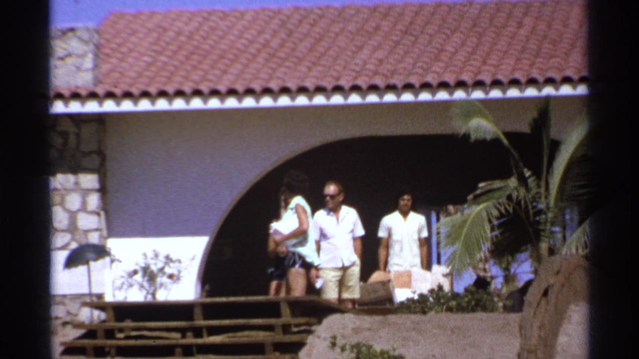 Adults stand near an arched villa walkway with a terracotta roof and stone wall.