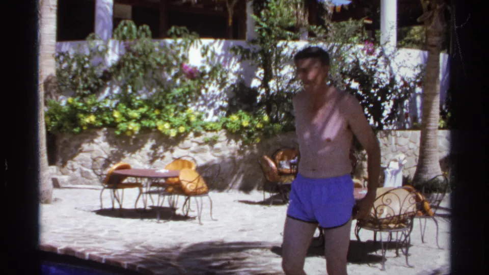 Near the end of the clip, the man passes close to the camera in the sunlit Cabo San Lucas courtyard with seating and plants behind him.