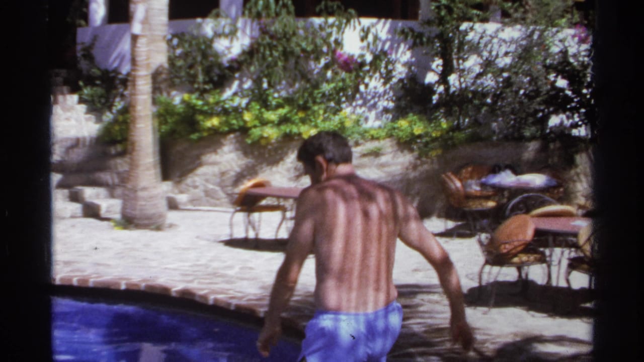 Man seen from behind near a swimming pool in a resort courtyard.