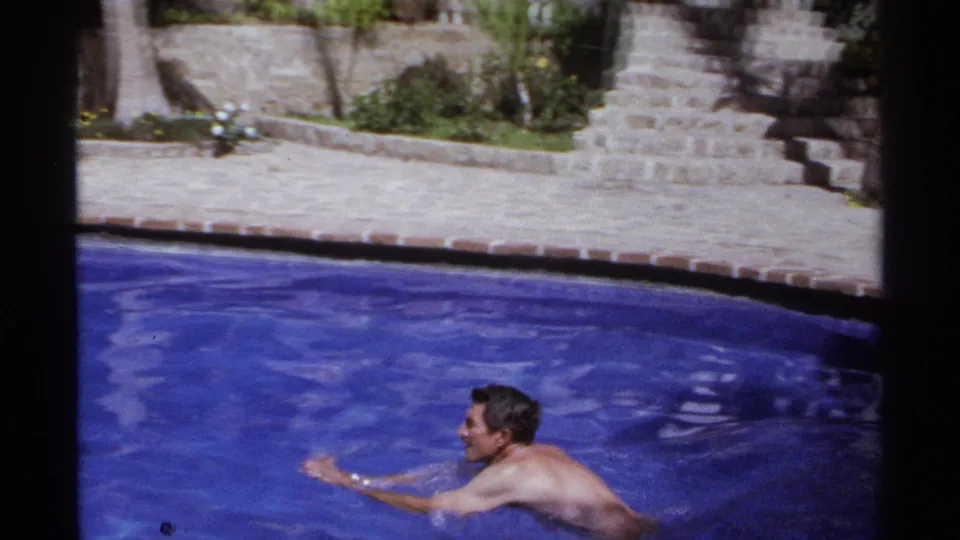 Two adult men swim in a blue resort pool in Cabo San Lucas, Mexico, in 1974 home-movie footage.