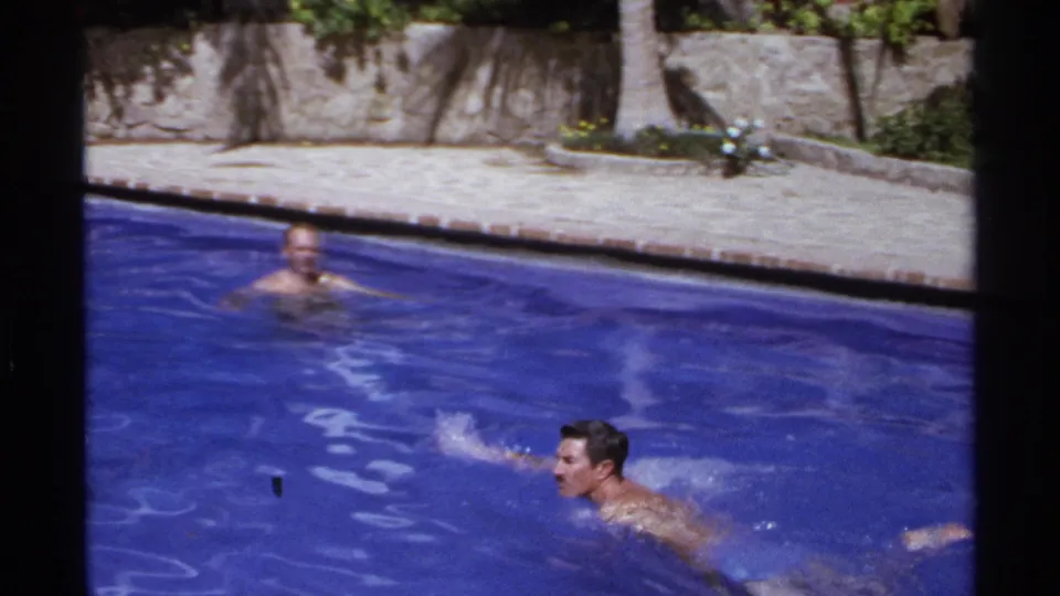 A man swims across the foreground while another adult swimmer looks on in a Cabo San Lucas resort pool.