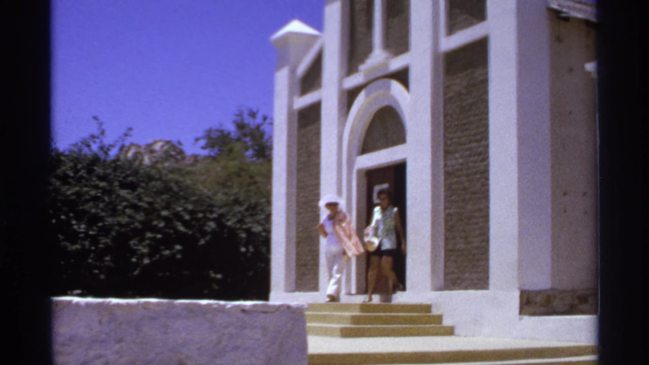 Two women stand near the steps of a white arched church entrance.