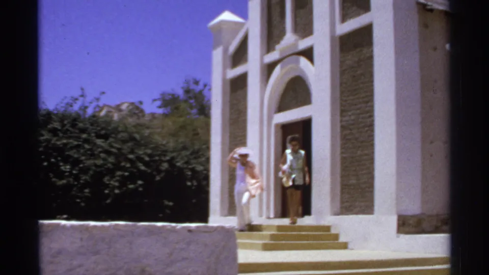 1974 Cabo San Lucas home-movie view of a woman by the church steps with another person visible in the doorway.