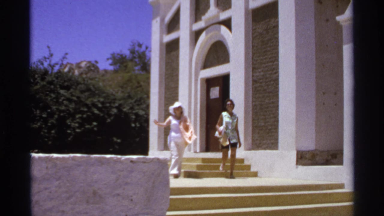 Two women stand near the steps of a white church with an arched doorway.