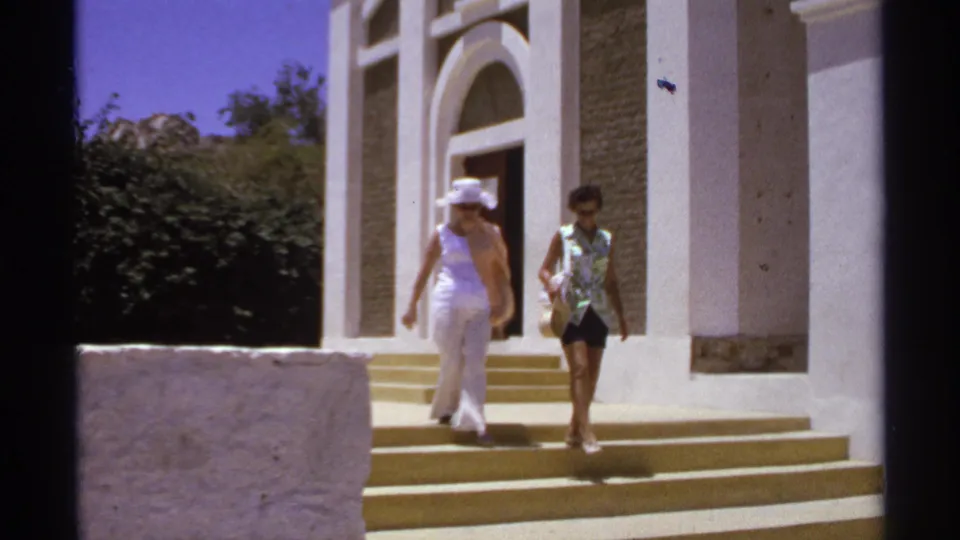 Near the end of the clip, two women descend the lower steps of the Cabo San Lucas church exterior in strong sunlight.