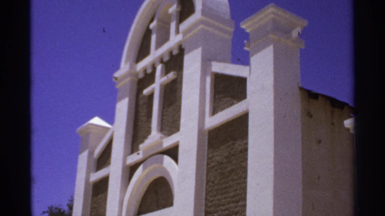 White church facade with arched openings and a cross against blue sky.
