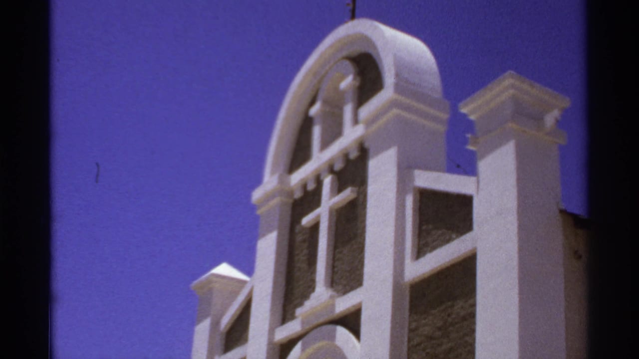 Upper church facade with cross, arched trim, and square pillars.