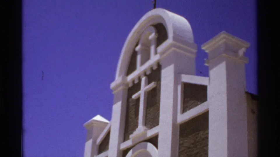 1974 Cabo San Lucas frame of the upper church facade, with white arched trim, a cross, dark wall panels, and clear blue sky.