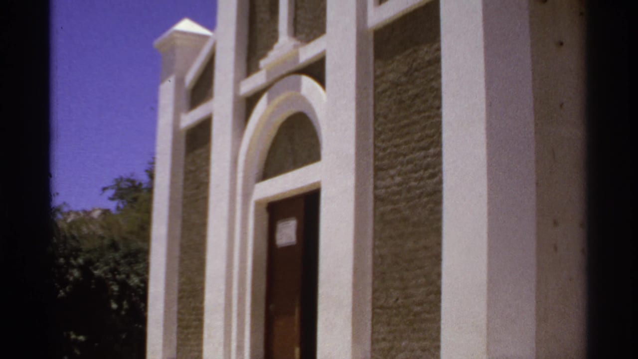Closer view of the church entrance with arched trim, cross, door, and trees.