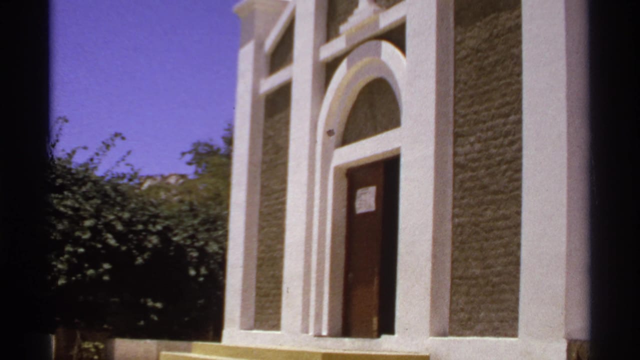 White arched doorway and steps beside shrubs under a blue sky.