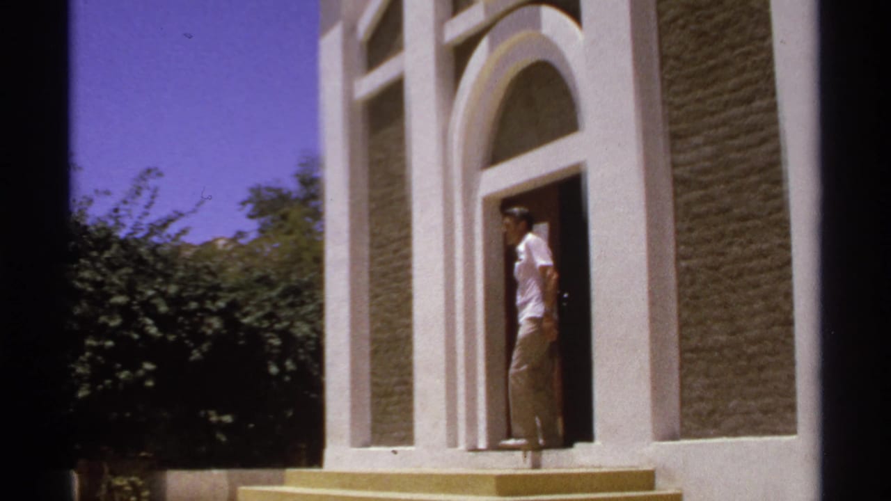Adult man standing in an arched doorway of a sunlit building.