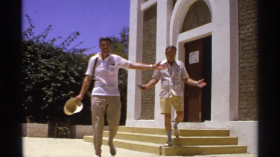 In the 1974 Cabo San Lucas clip, the man in a white polo approaches the camera with a straw hat as the second man follows from the steps.