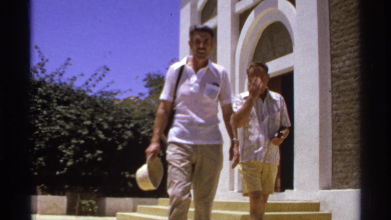 Two men walk down steps outside a white building with arched doorways.