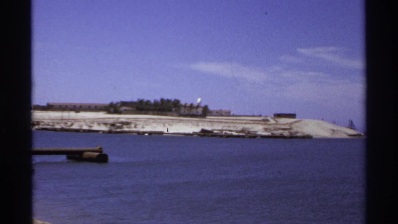 Blue sea facing a pale shoreline with low buildings and a small pier edge.