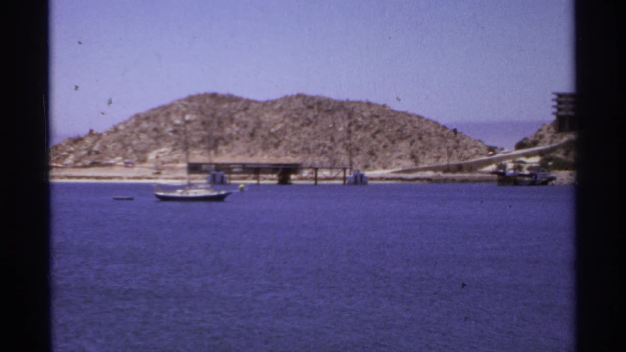 Sailboat floating near a pier with a rocky hill behind it.