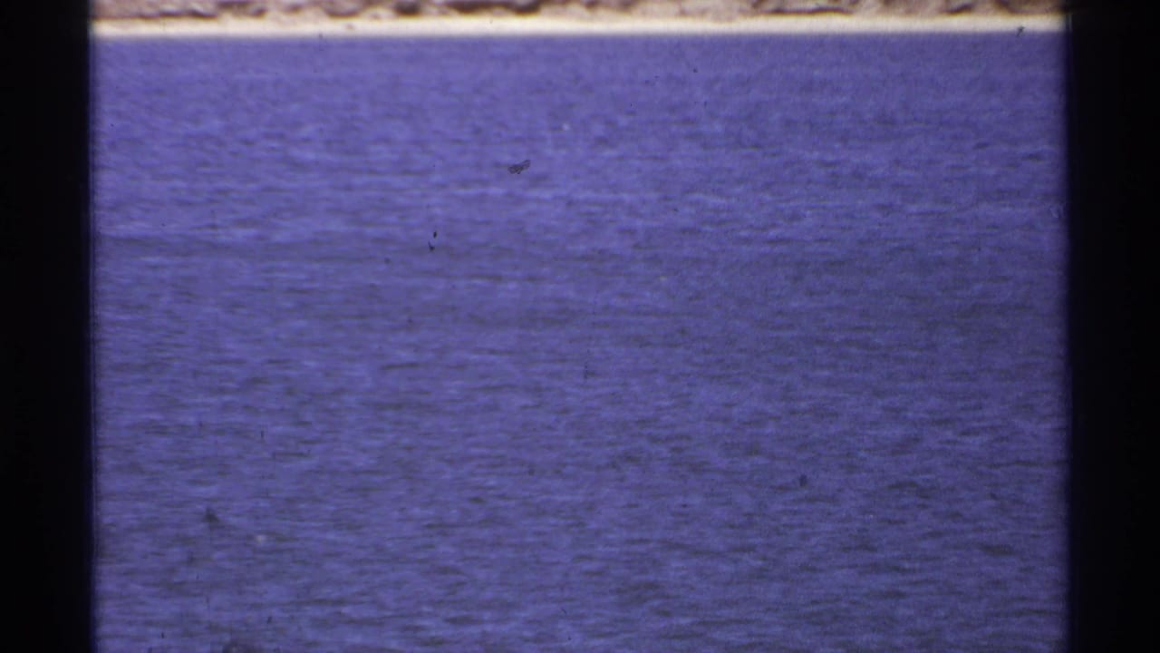 1974 8mm Cabo San Lucas footage begins on blue ocean water with a distant pale shoreline and visible film-frame edges.