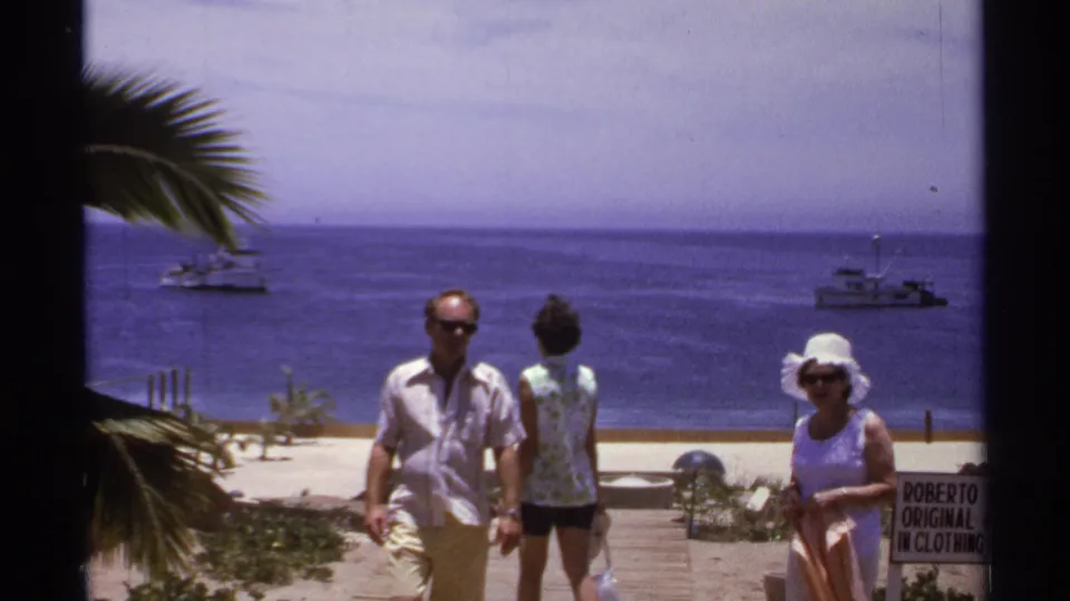 Three adults are visible at the Cabo San Lucas overlook, with boats on the blue sea and a small Roberto clothing sign at the right edge.