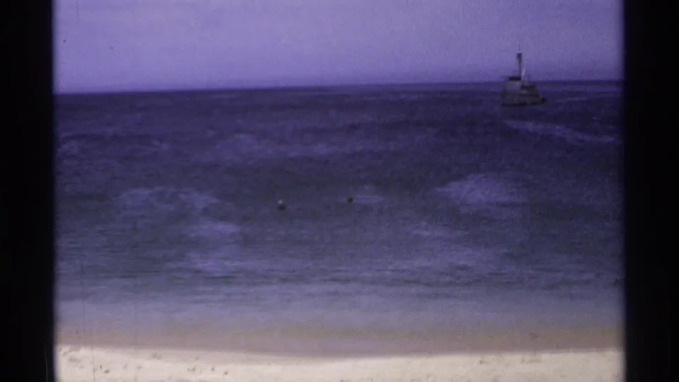 1974 Cabo San Lucas home-movie view of the sandy shore, deep blue water, and small boats offshore without people in the frame.