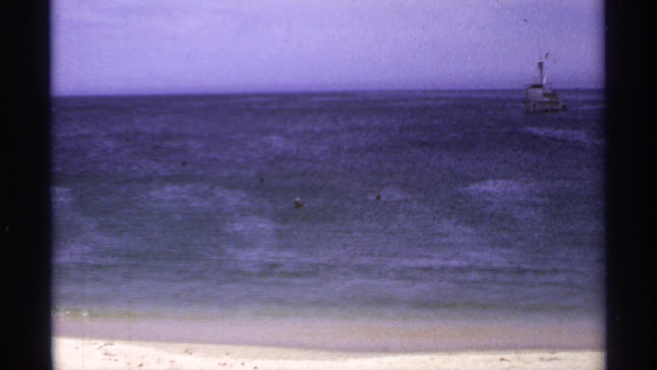 Distant boat on the ocean beyond a sandy beach and low surf.