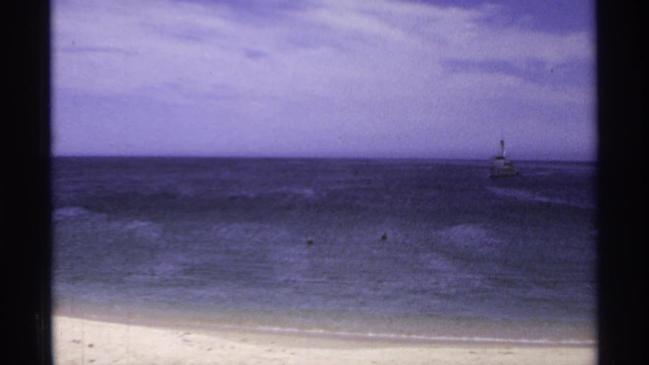 Dark ocean seen from a sandy beach with a small distant structure on the horizon.
