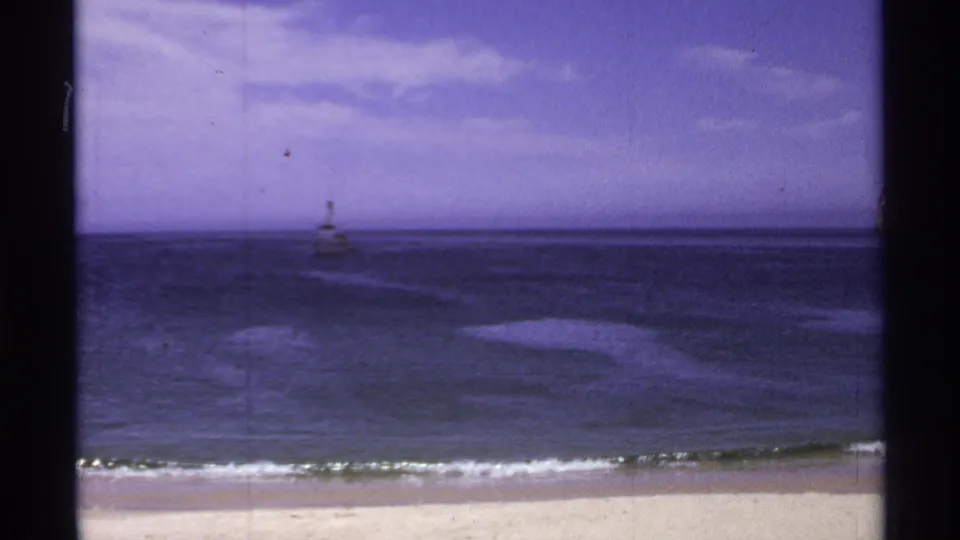 1974 coastal home-movie frame showing gentle surf, open water, and a small offshore beacon at Cabo San Lucas.