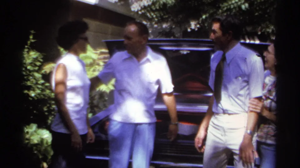 1974 La Paz travel footage shows several adults talking beside a classic car with its trunk raised.